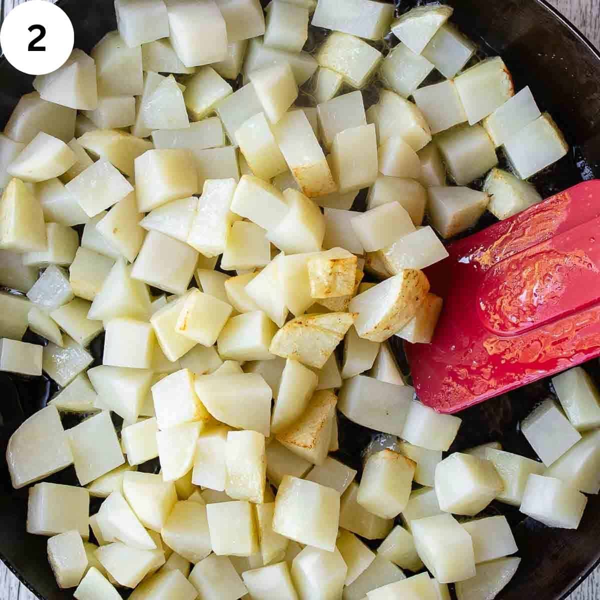 Stirring cubed fried potatoes with a spatula.