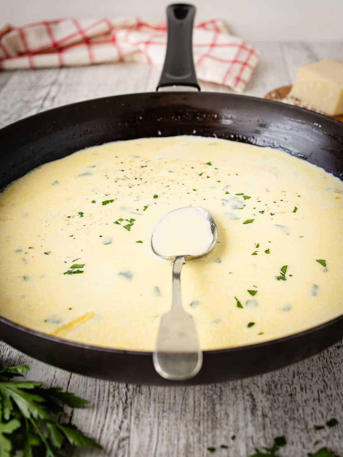 A close-up of a skillet filled with Garlic Parmesan sauce, with a metal spoon resting in it.