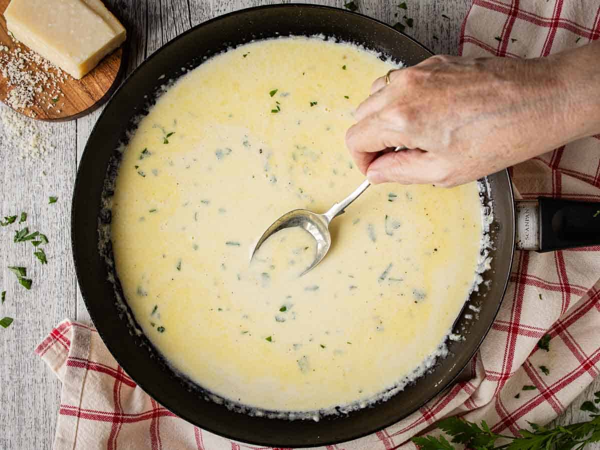 Creamy sauce being stirred in a skillet.