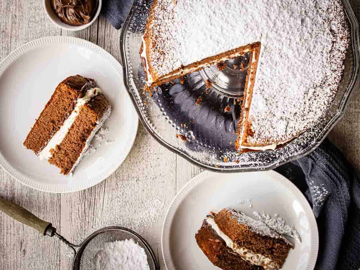 Overhead view of two layer chocolate cake filled with chocolate and cream with two wedges removed and on plates.