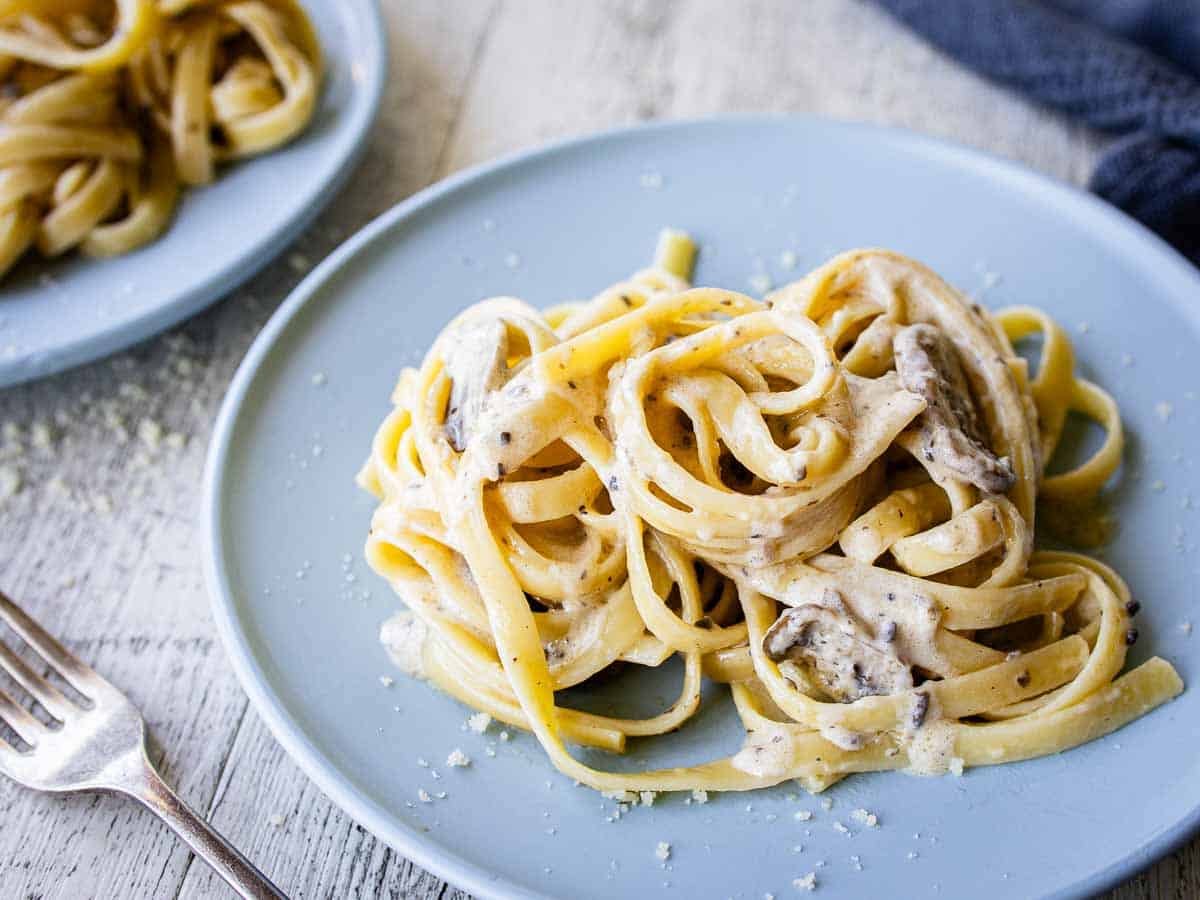 Fettuccini with black truffle cream sauce on a blue plate.