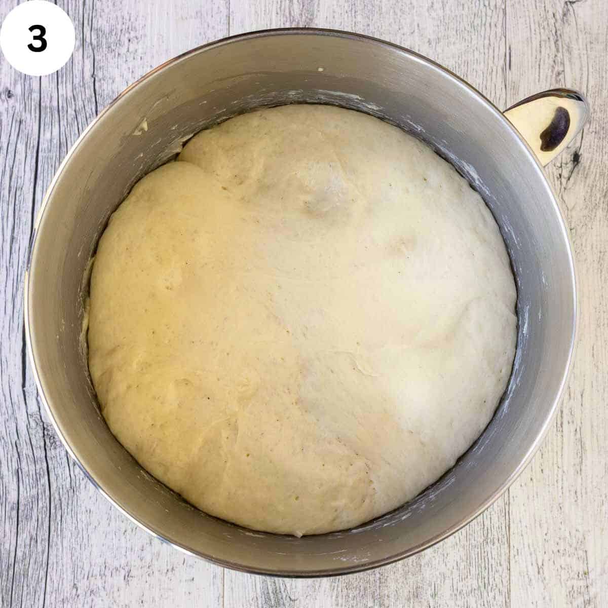 Risen bread dough in a stainless steel bowl.