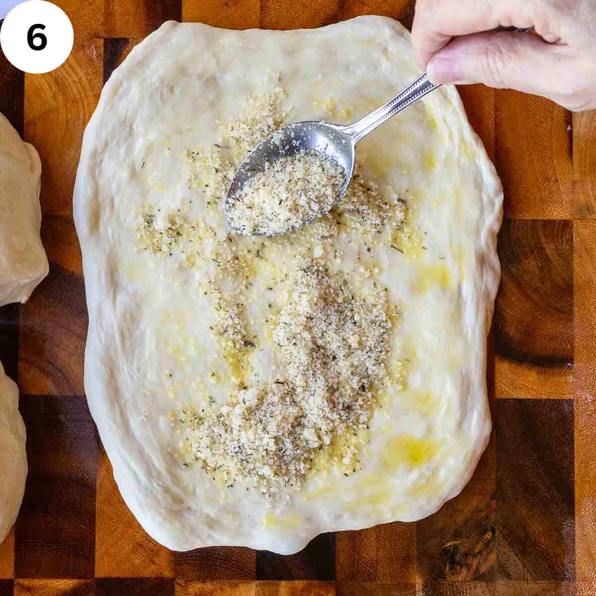 Sprinkling cheese and herb mixture on flattened bread dough.