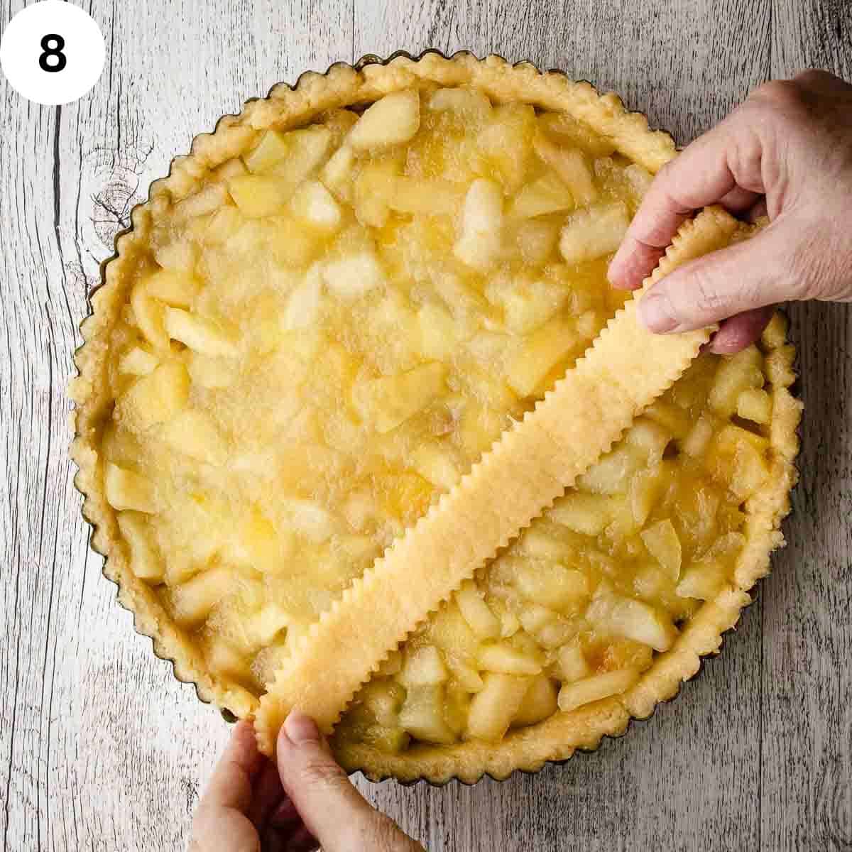 Laying a strip of pastry over apples in a tart pan.