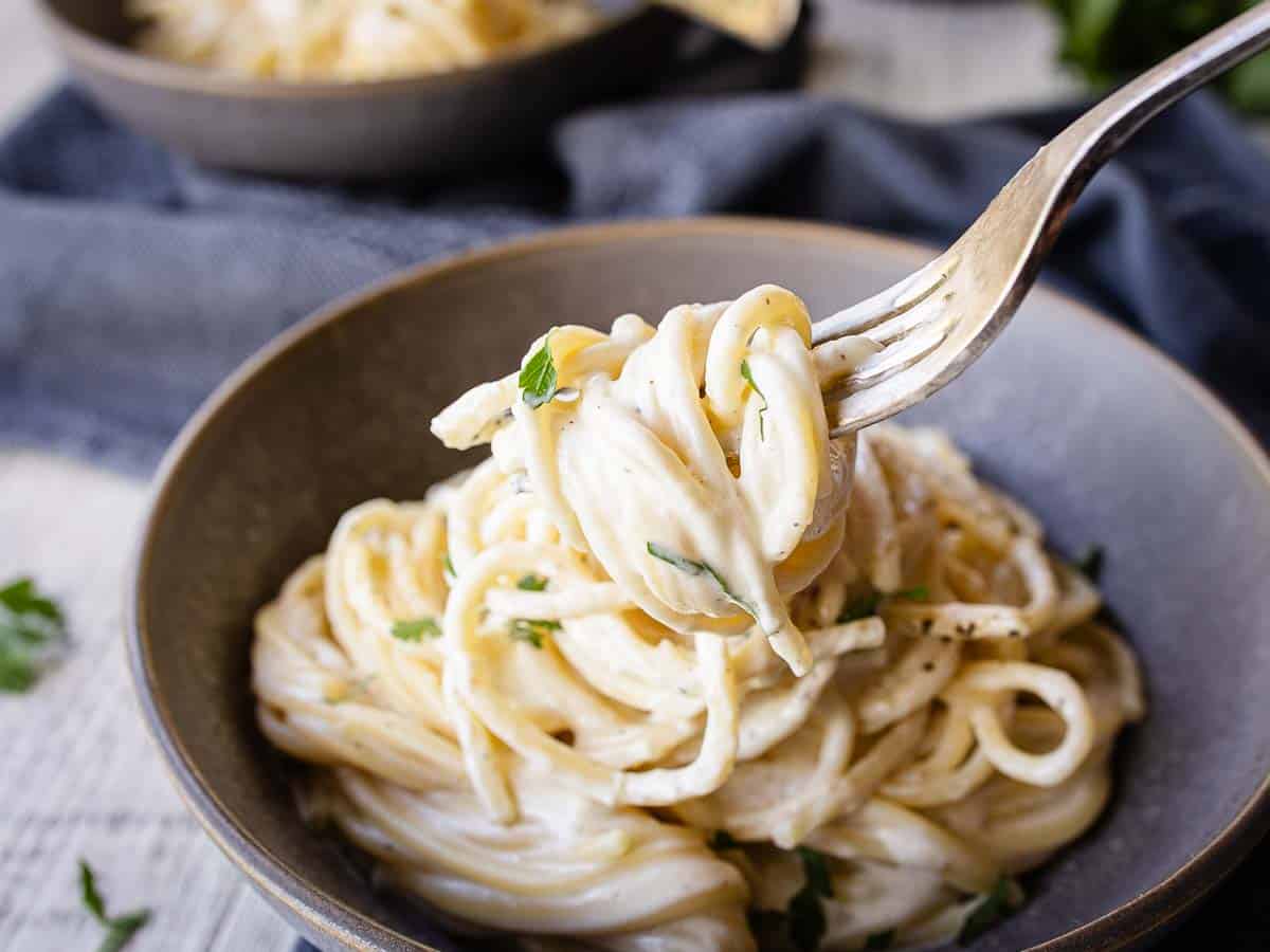 Close up of cream cheese spaghetti in a bowl with some on a fork.