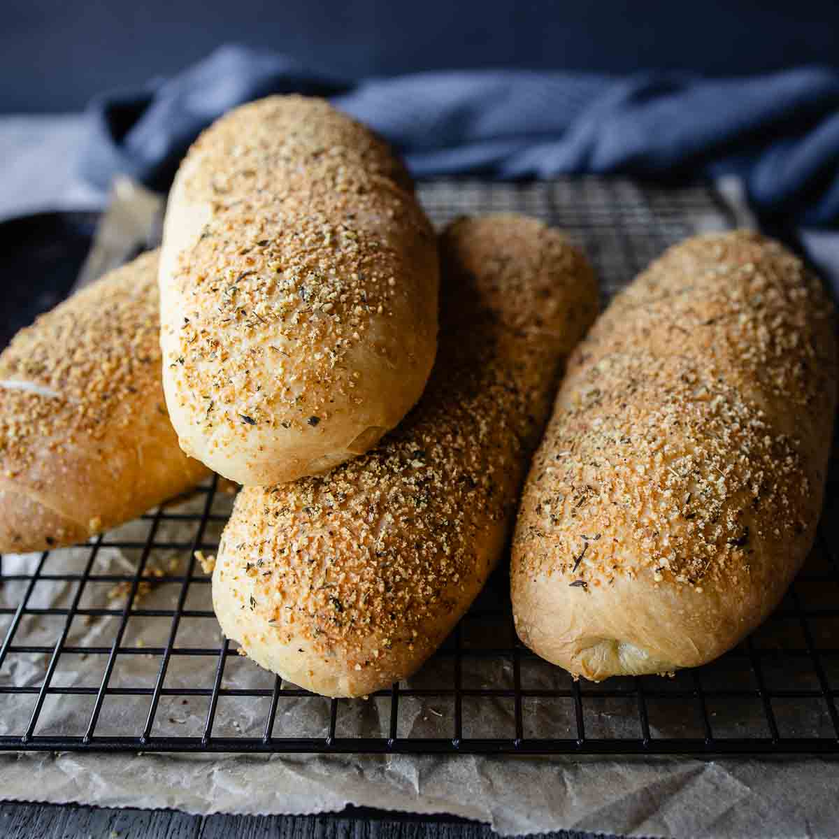 Italian cheese and herb bread loaves piled up on a wire rack.