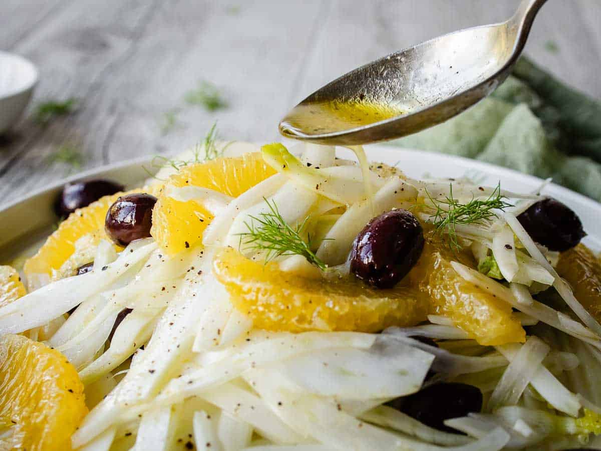 Salad dressing being poured over fennel orange salad.