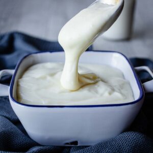 Besciamella sauce pouring off a spoon and into a bowl.