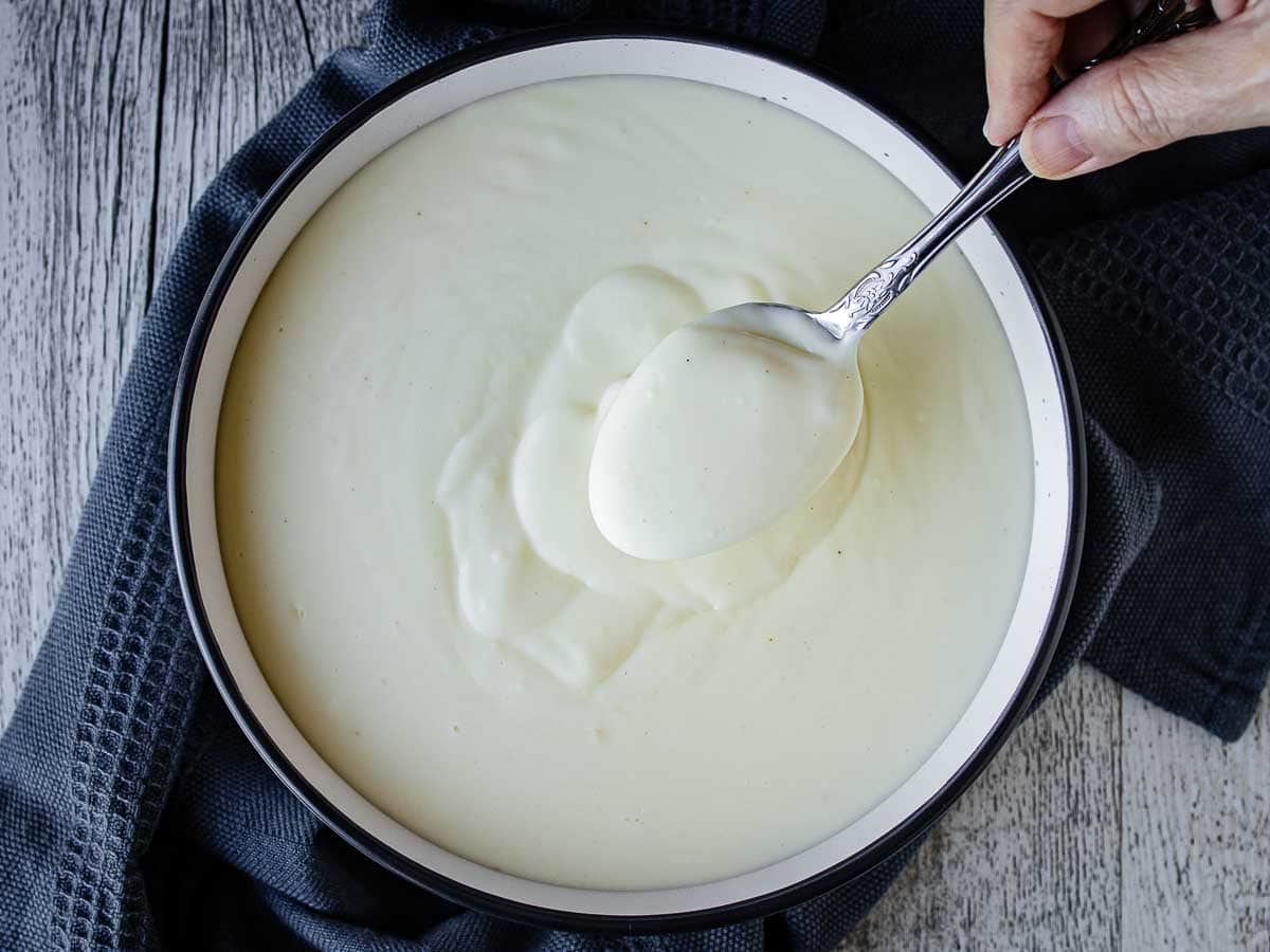 Overhead view of bechamel sauce being spooned into a bowl.