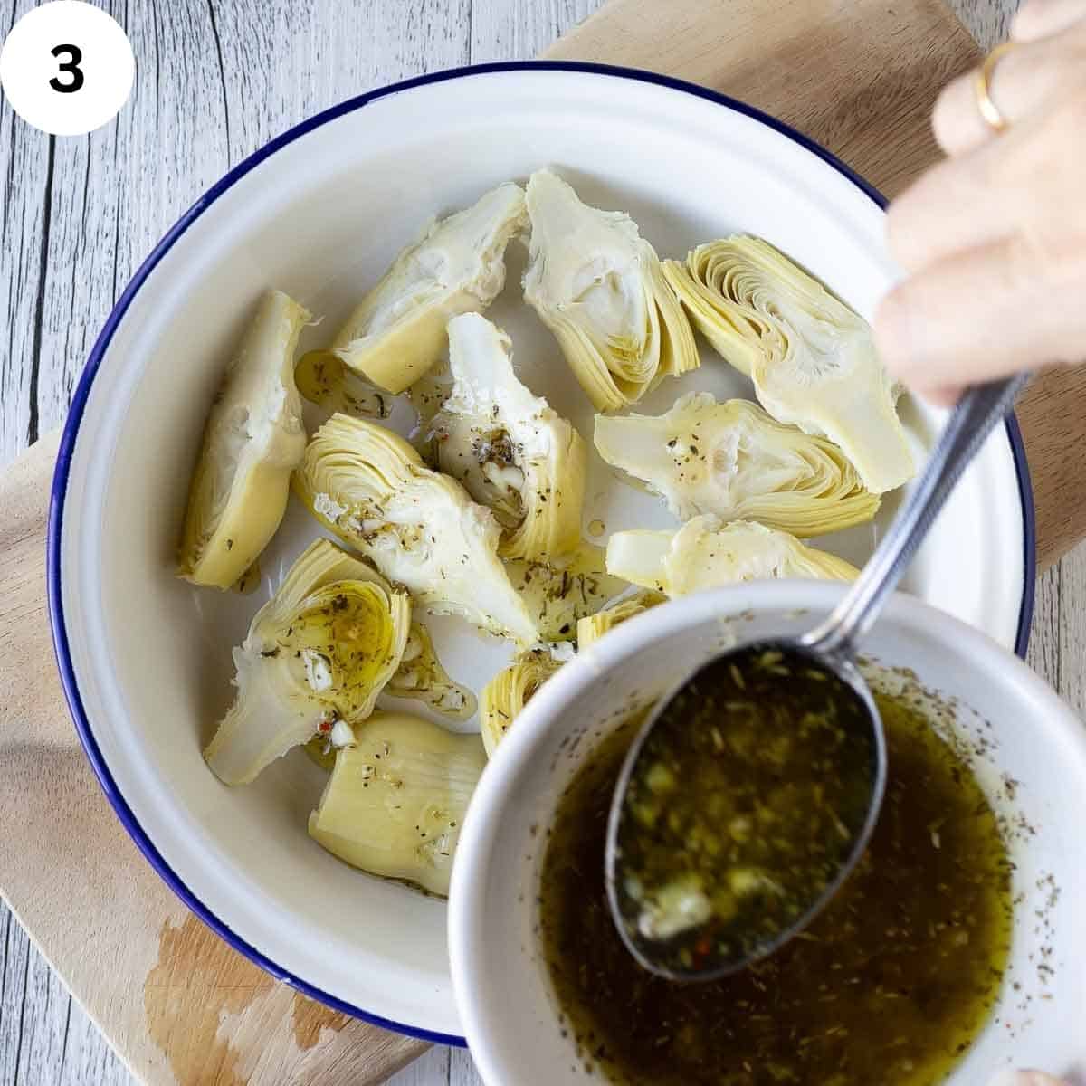 Spooning dressing onto canned artichokes in a dish.