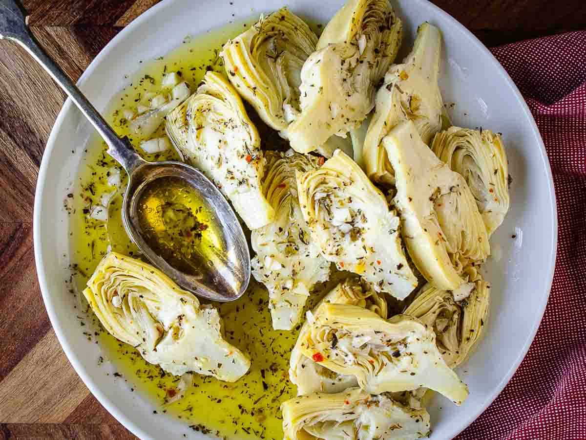 Canned artichokes halves on a plate dressing with herby marinade.