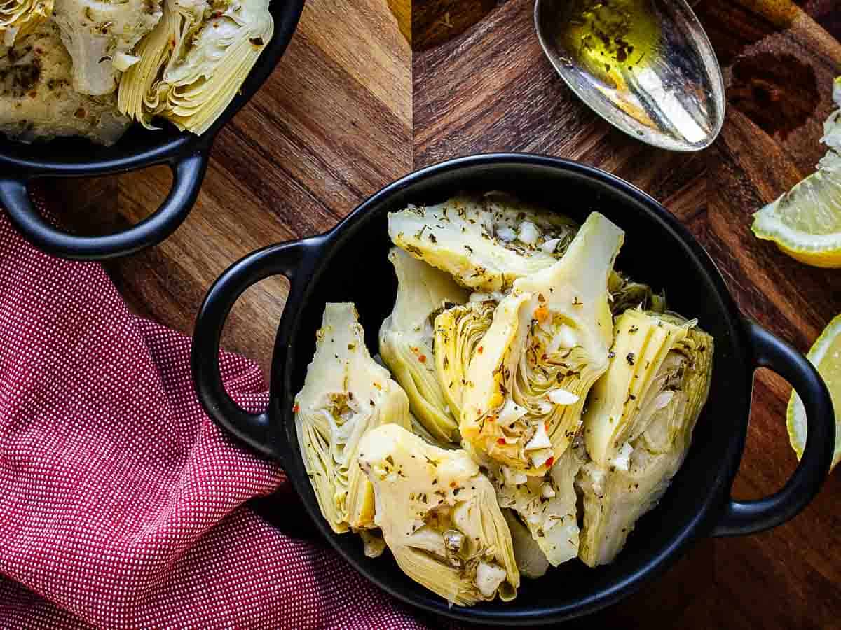 Canned artichokes hearts marinated in herby dressing in a bowl viewed from above.