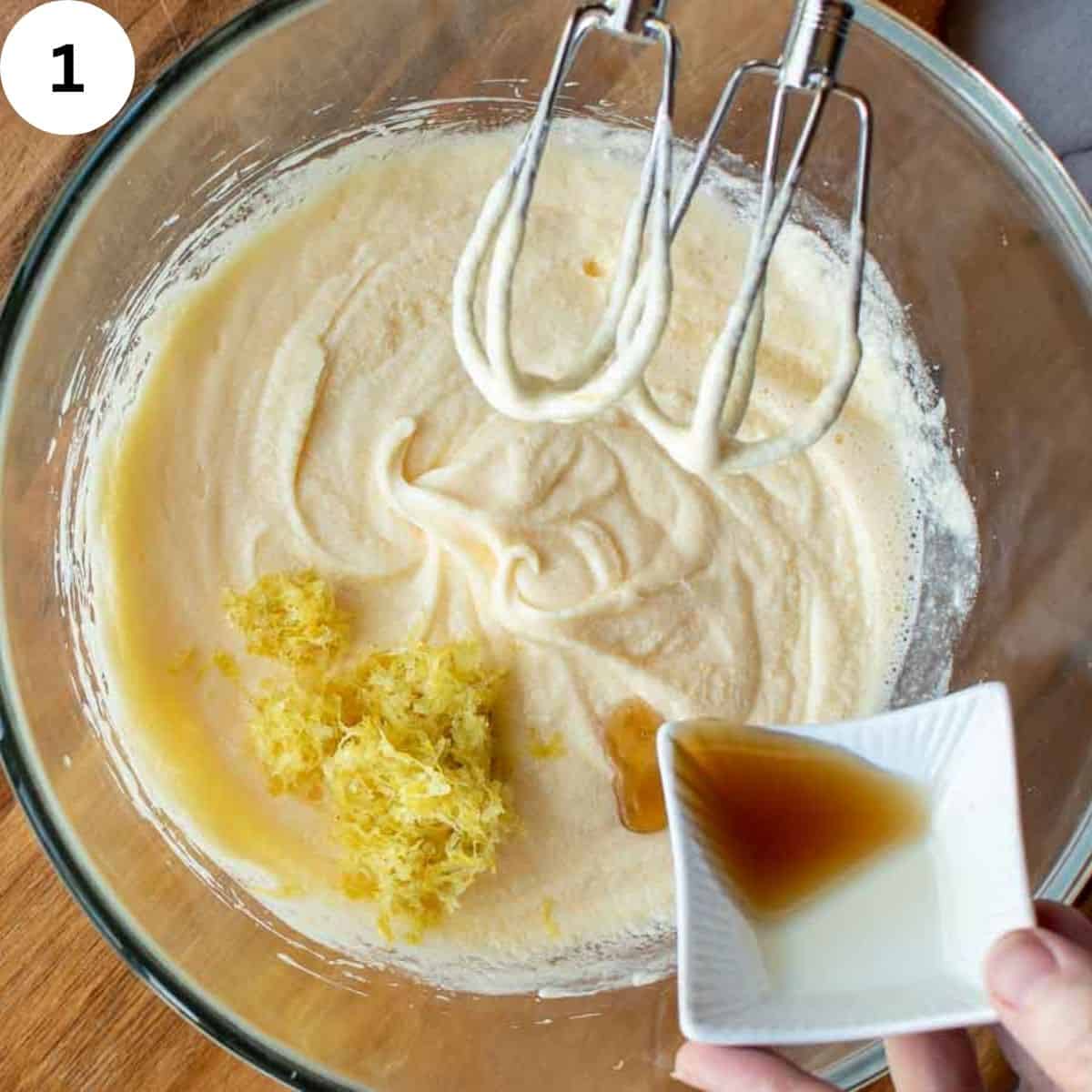 Creamy batter in a glass bowl with grated lemon zest and vanilla extract being added.