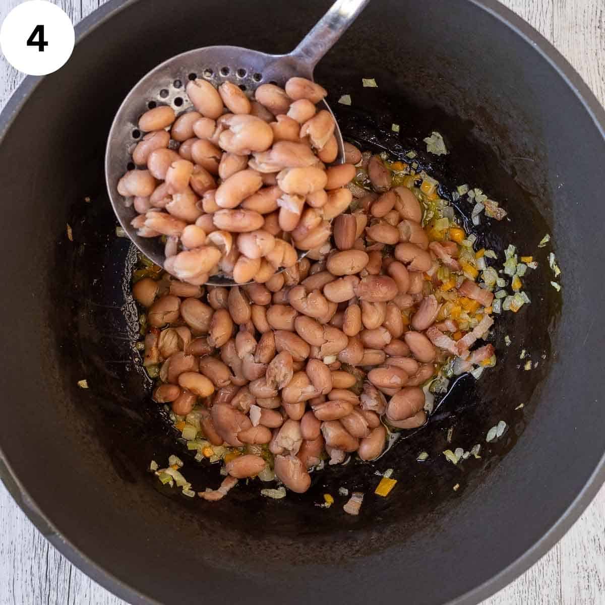 Cooked borlotti beans being added to a saucepan.