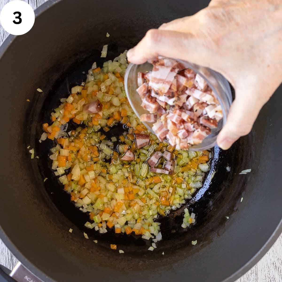 Chopped pancetta being added to a saucepan of sauteed chopped vegetables.