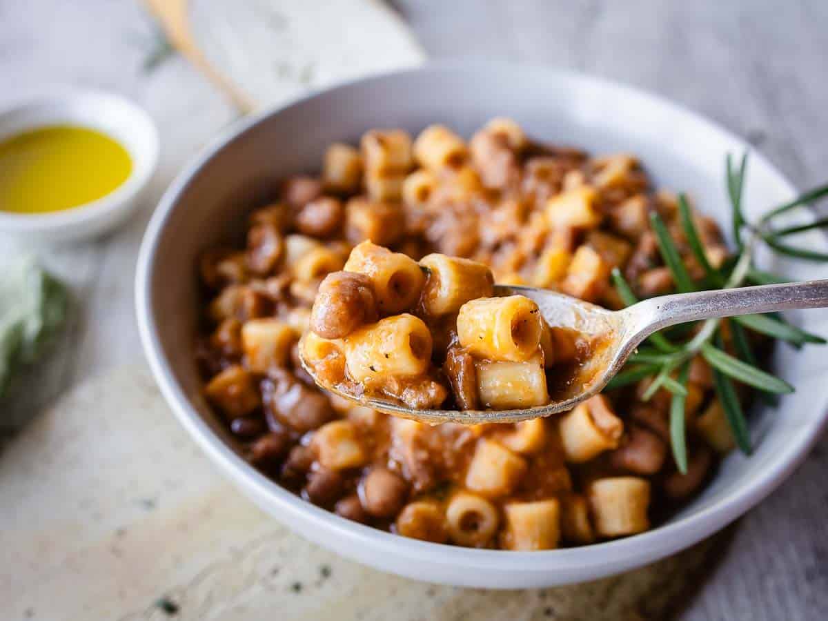 A spoonful of pasta and bean stew being raised above the bowlful of stew.