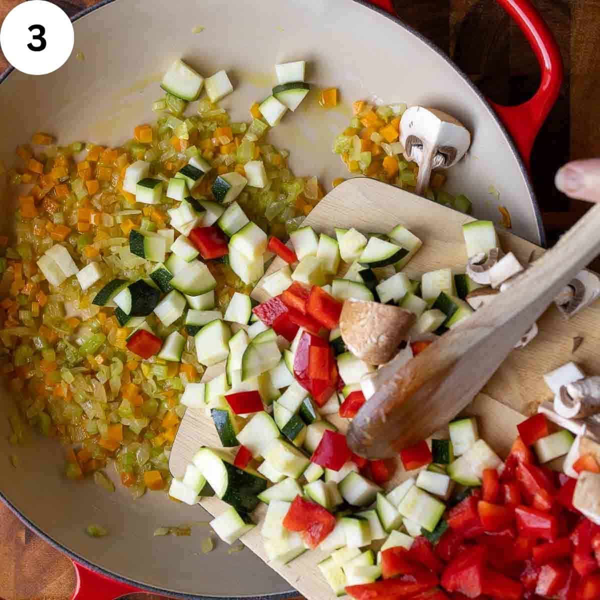 Adding chopped mix of vegetables to a pan of cooked chopped onion, carrot and celery.