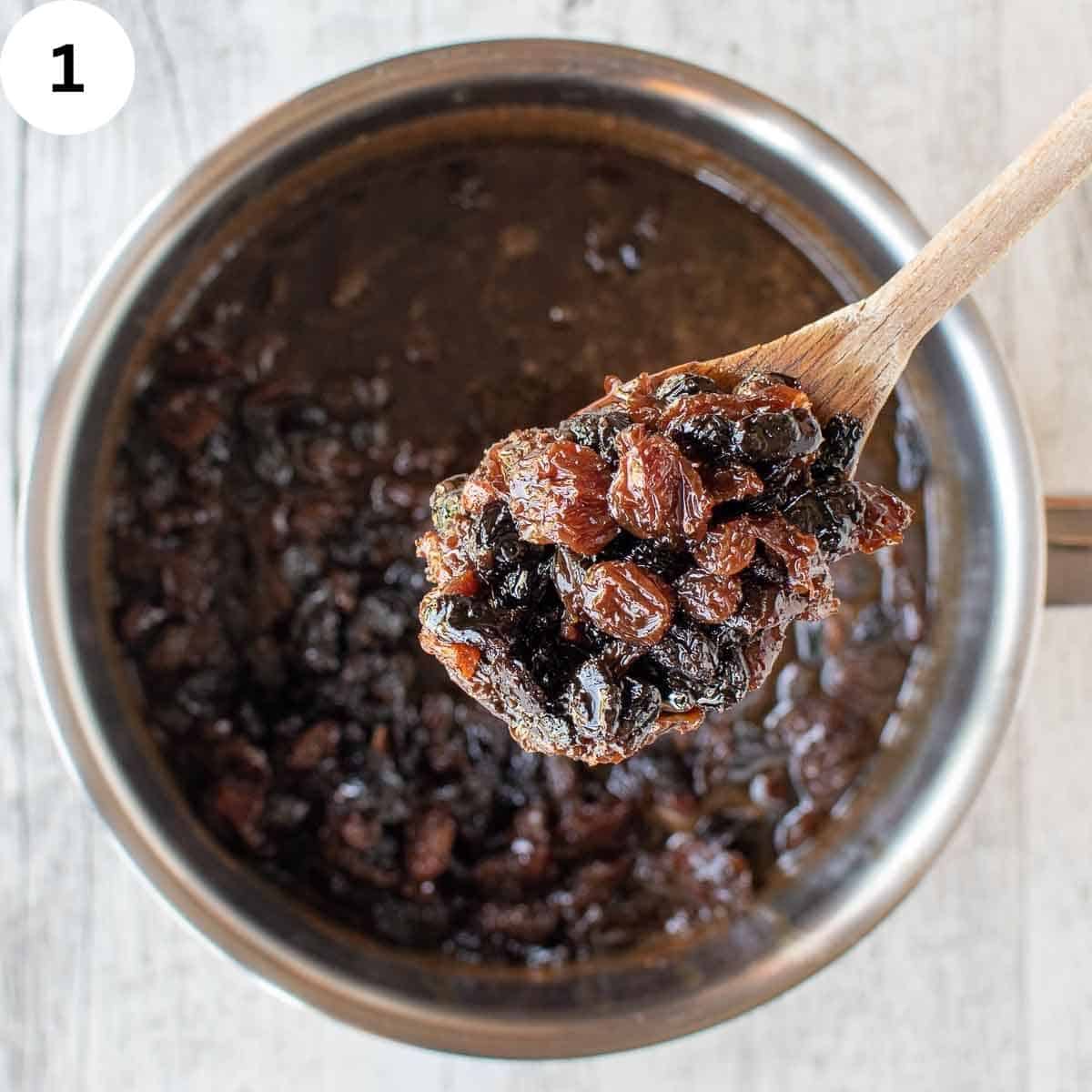 Boiled mixed dried fruit in a saucepan with a spoonful being held up close.
