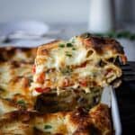 A slice of vegetable lasagna with white sauce being lifted out of a baking dish.
