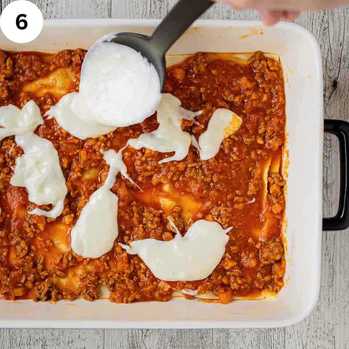Thick white sauce being dolloped over meat sauce.