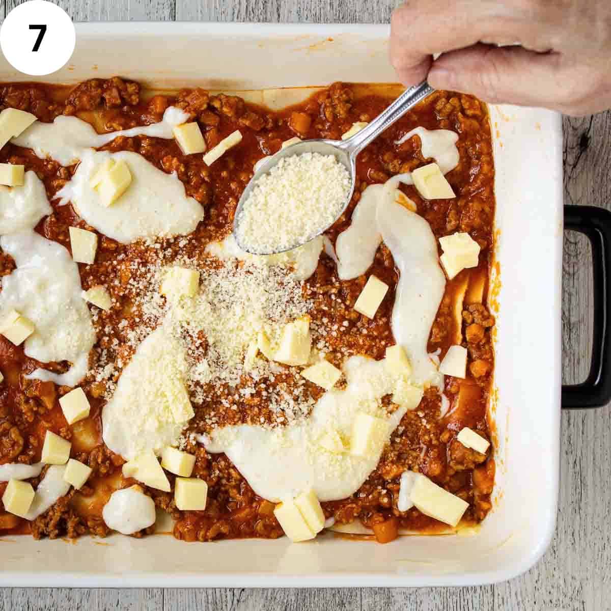 Sprinkling grated cheese over a layer of lasagna.