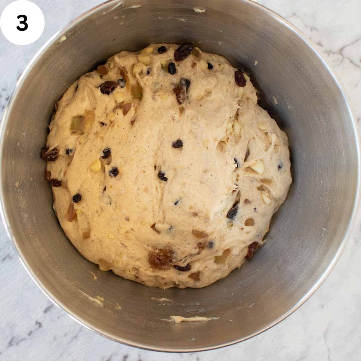 Ball of dough with dried fruit through it in a stainless steel bowl.