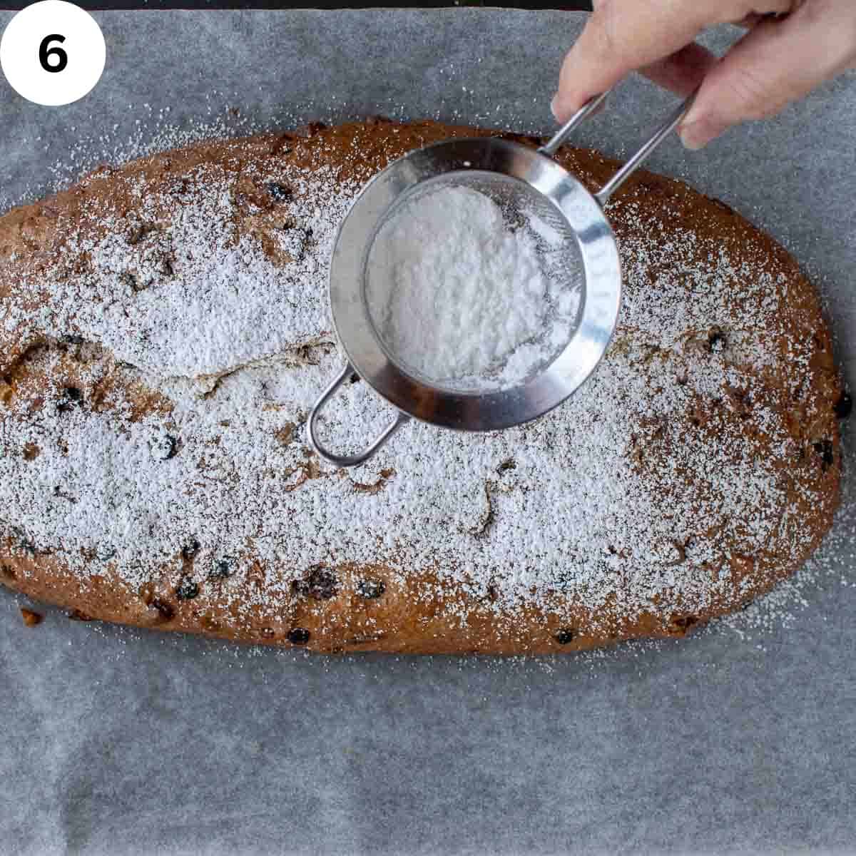 Powdered sugar being dusted over fruited baked bread.