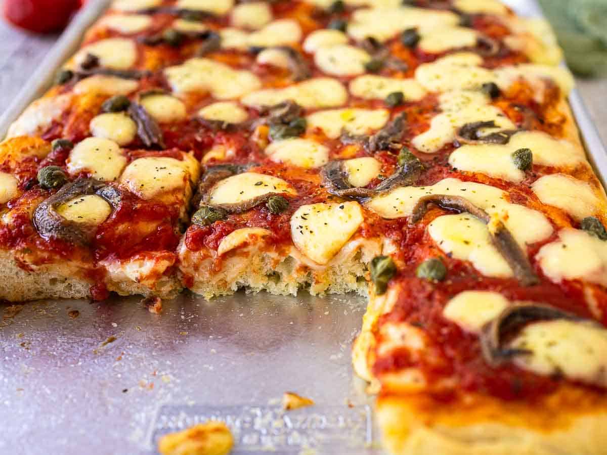 Rectangular pizza that has been cut and some slices removed.