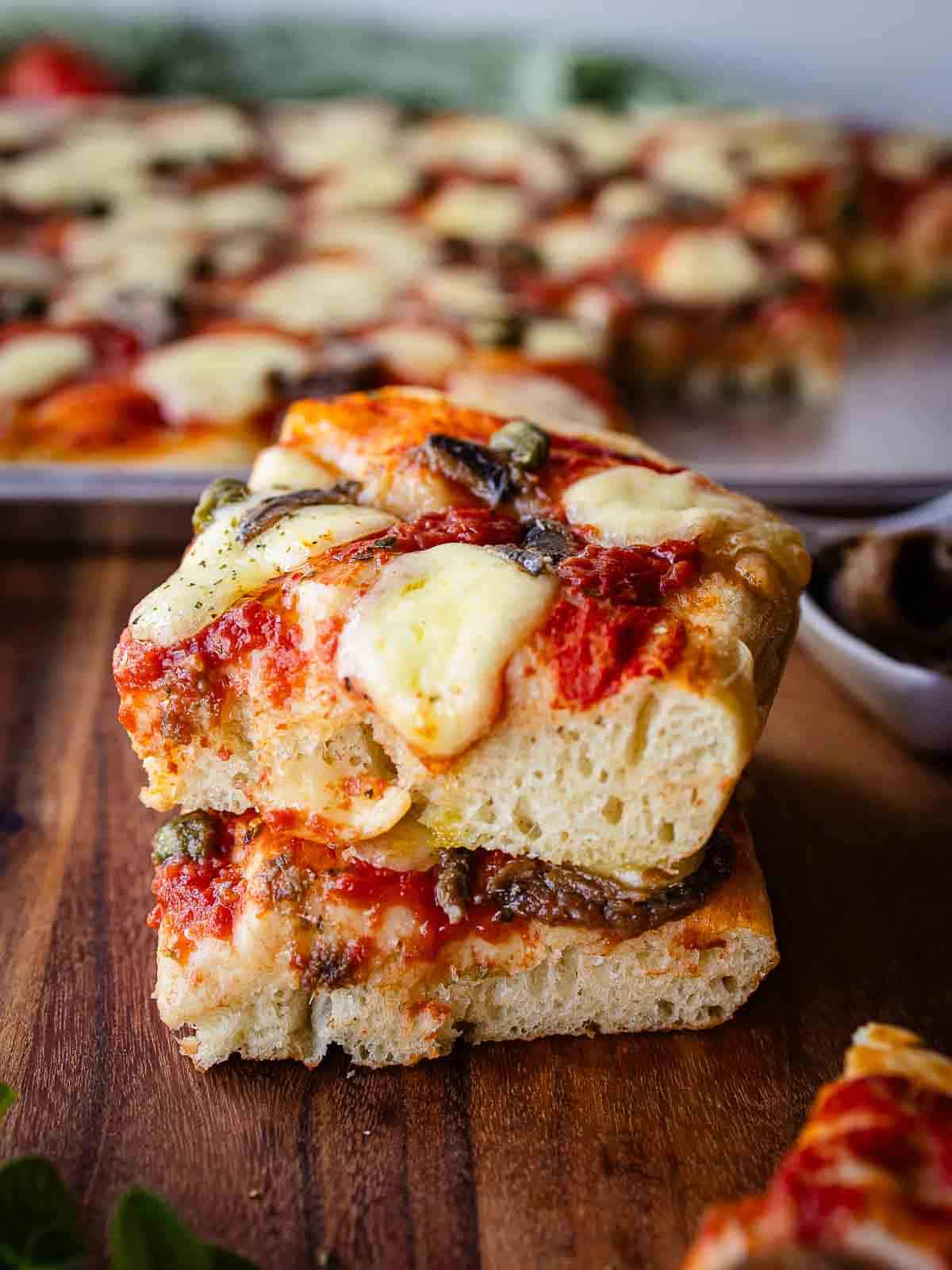 Two squares of Anchovy Pizza stacked on top of one another.