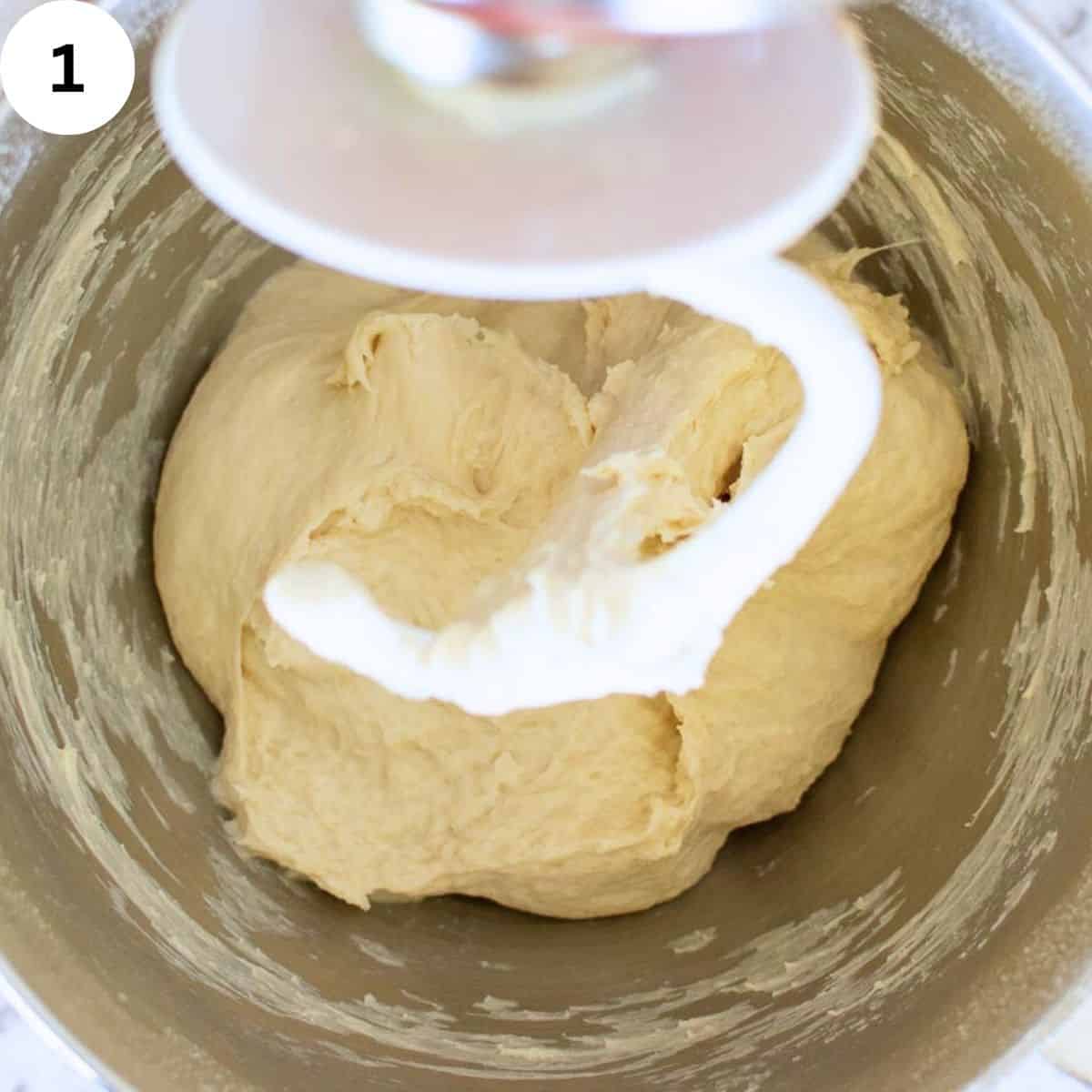 Dough hook attachment for stand mixer over head bread dough in a stainless steel bowl.