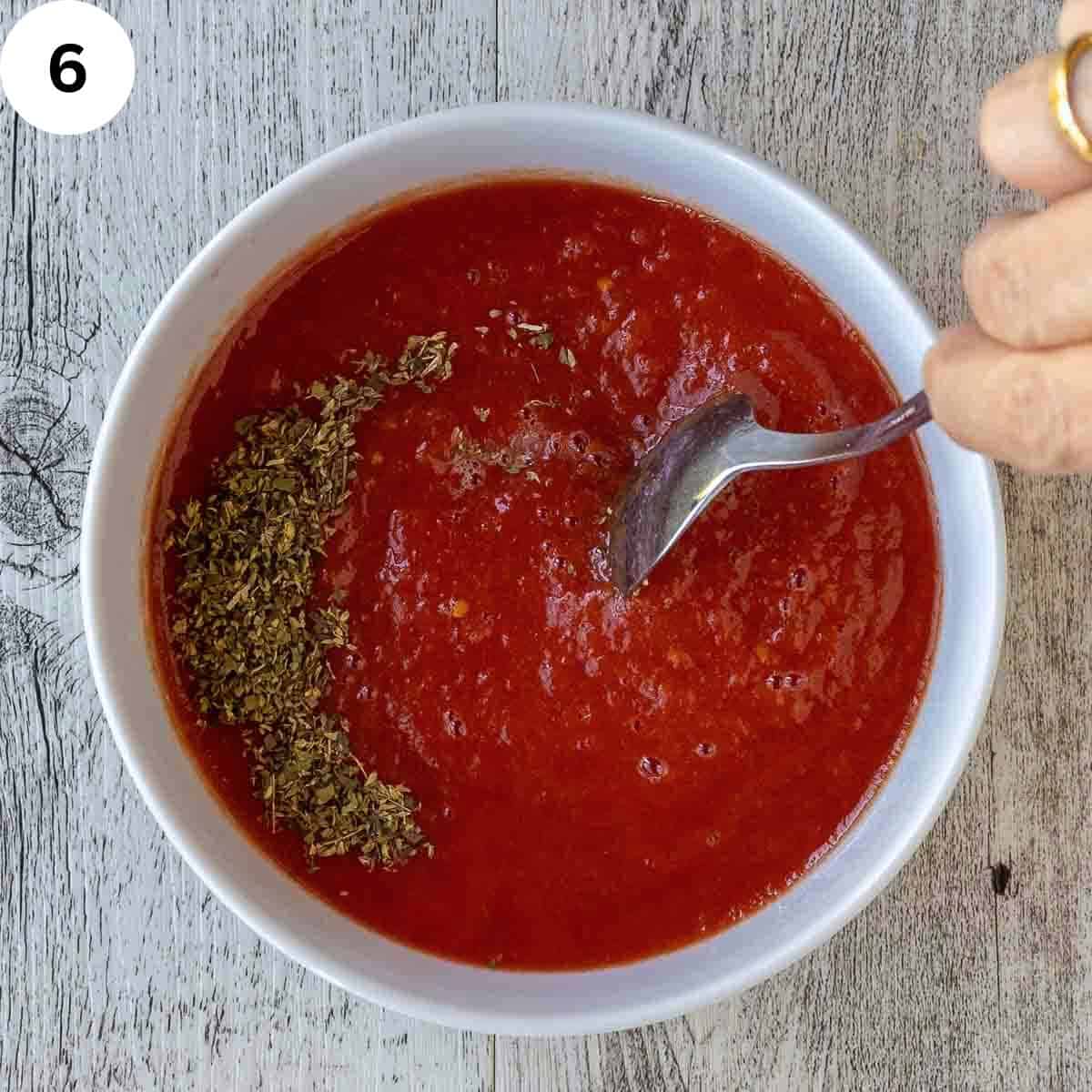Stirring dried herbs into tomato puree.