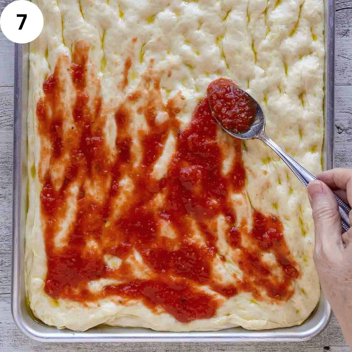 Spreading tomato puree over pizza dough in a rectangle pan.