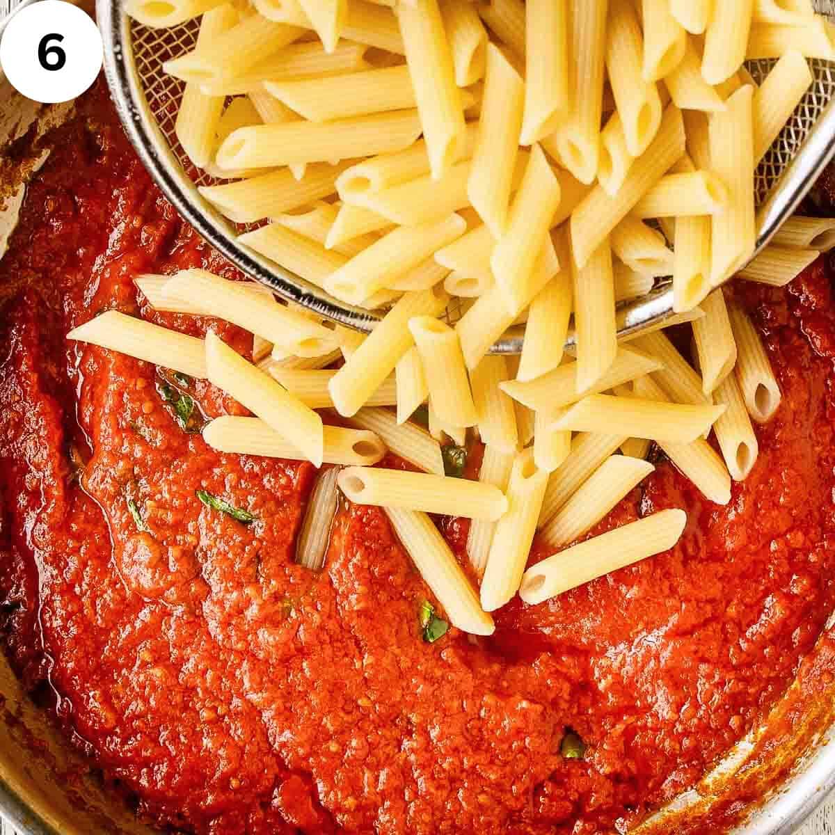 Cooked penne pasta being tipped into tomato sauce.