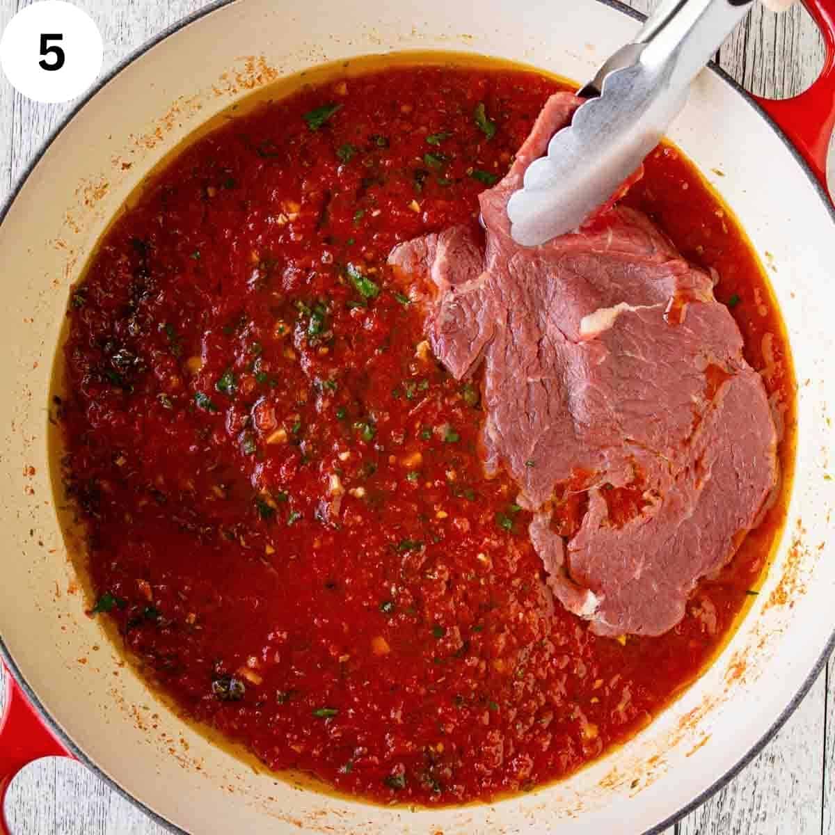 Adding raw thin steaks to tomato puree in a pan.