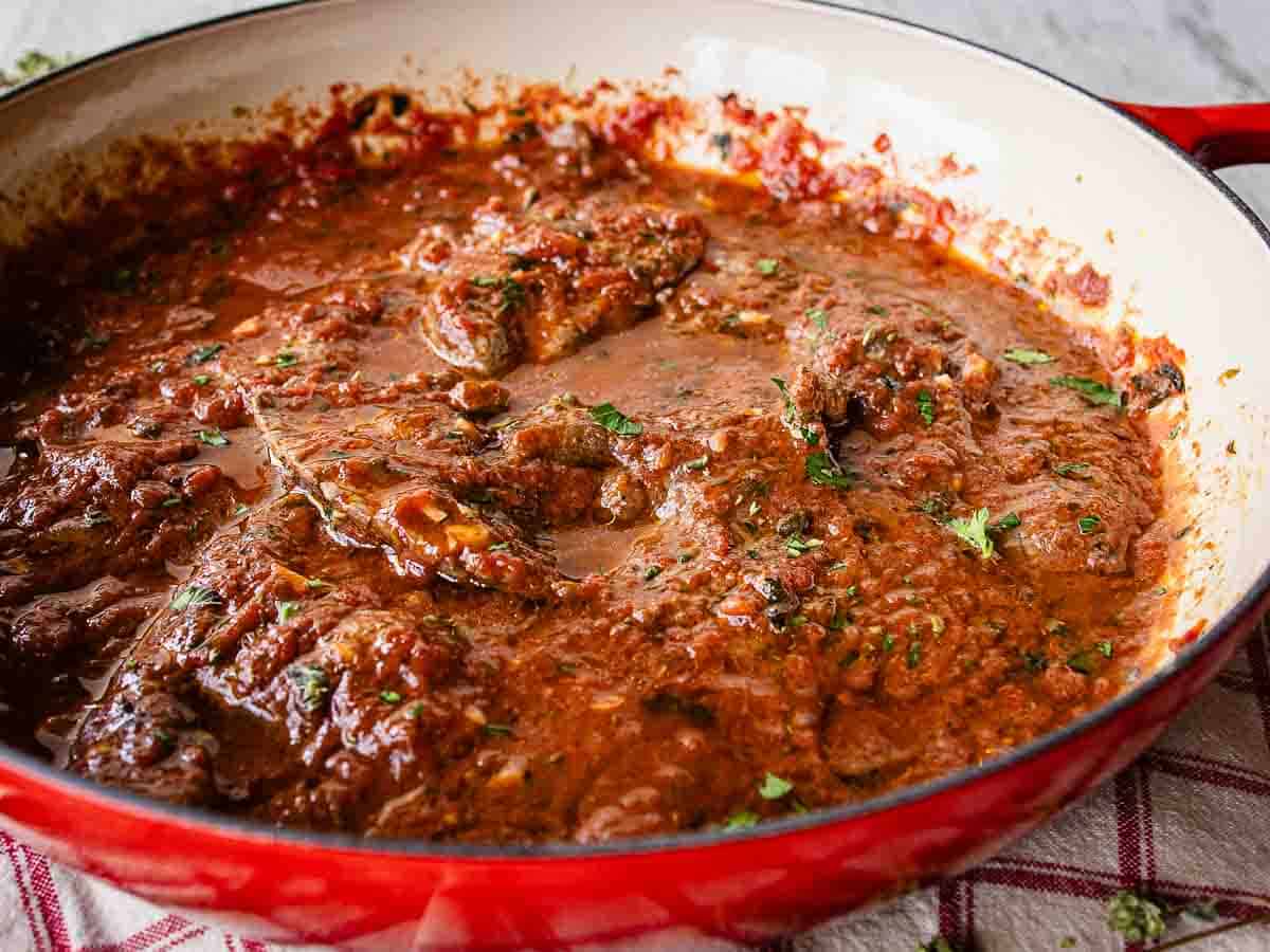 Cooked tomato gravy smoothering steaks in a skillet.