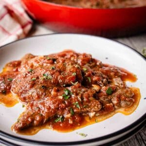 Steak Pizzaiola on a plate with a pan full at the back.
