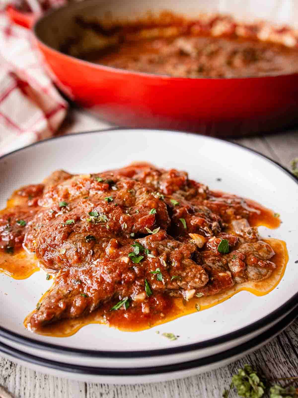 Steak Pizzaiola on a plate with a pan full at the back.