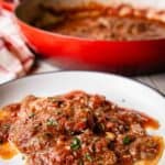 Steak Pizzaiola on a plate with a pan full at the back.