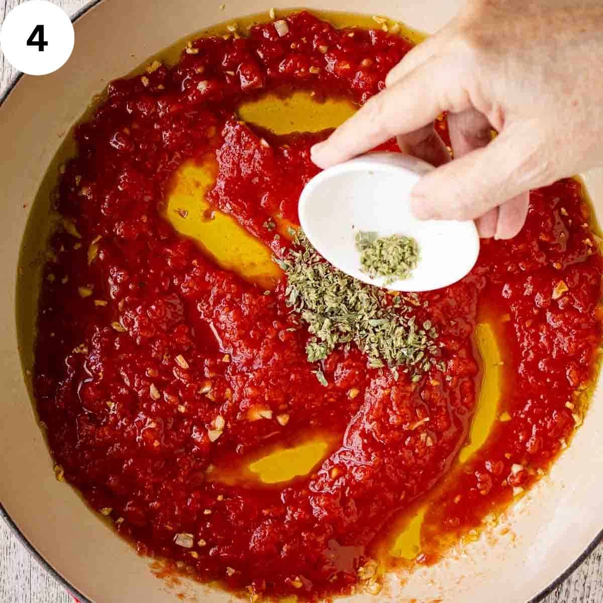 Dried herbs being sprinkled onto tomato puree in a pan.