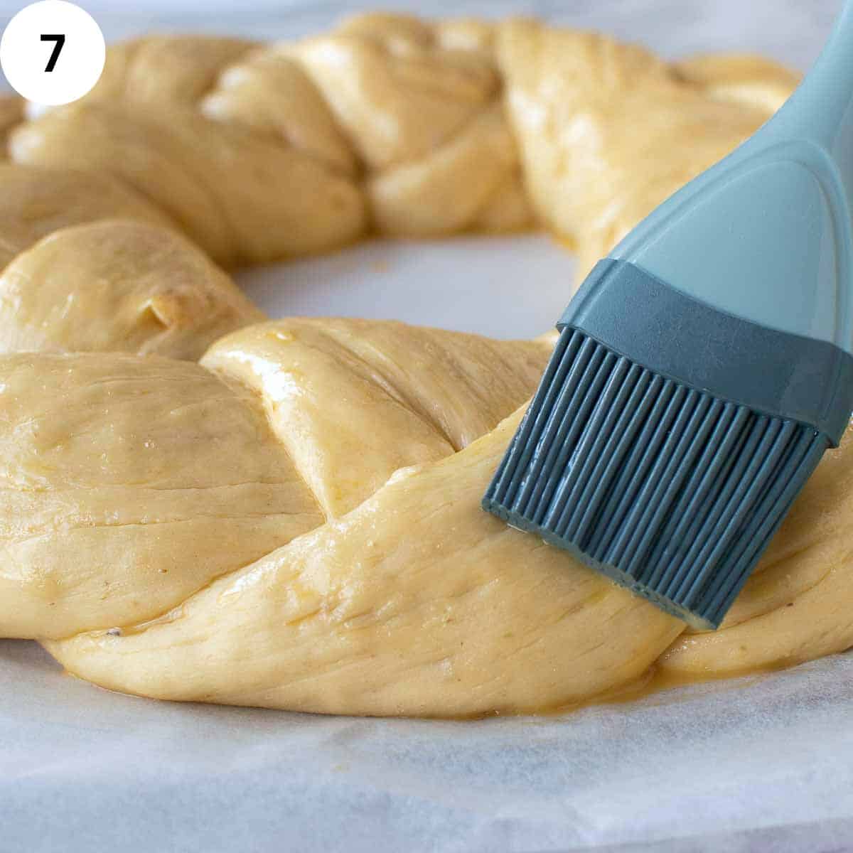 A brush brushing egg wash onto braided dough.
