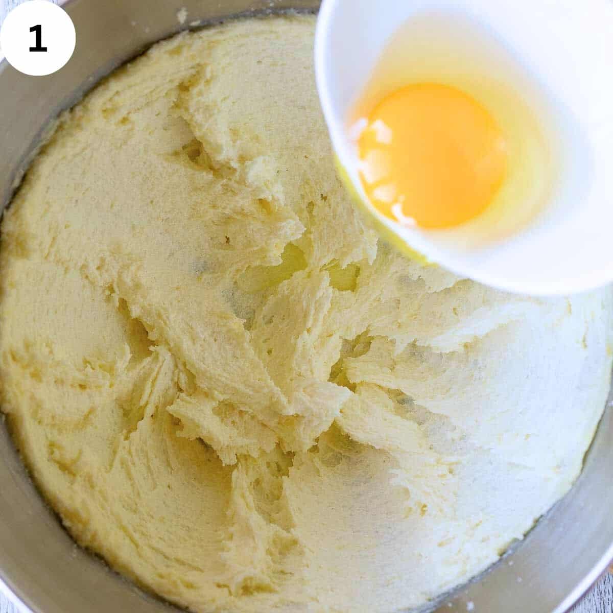 An egg being added into creamy butter and sugar mixture.