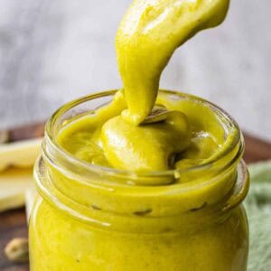 A pistachio cream recipe prepared and being spooned into a glass jar.