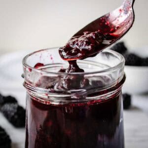 Blackberry compote being spooned into a glass jar.