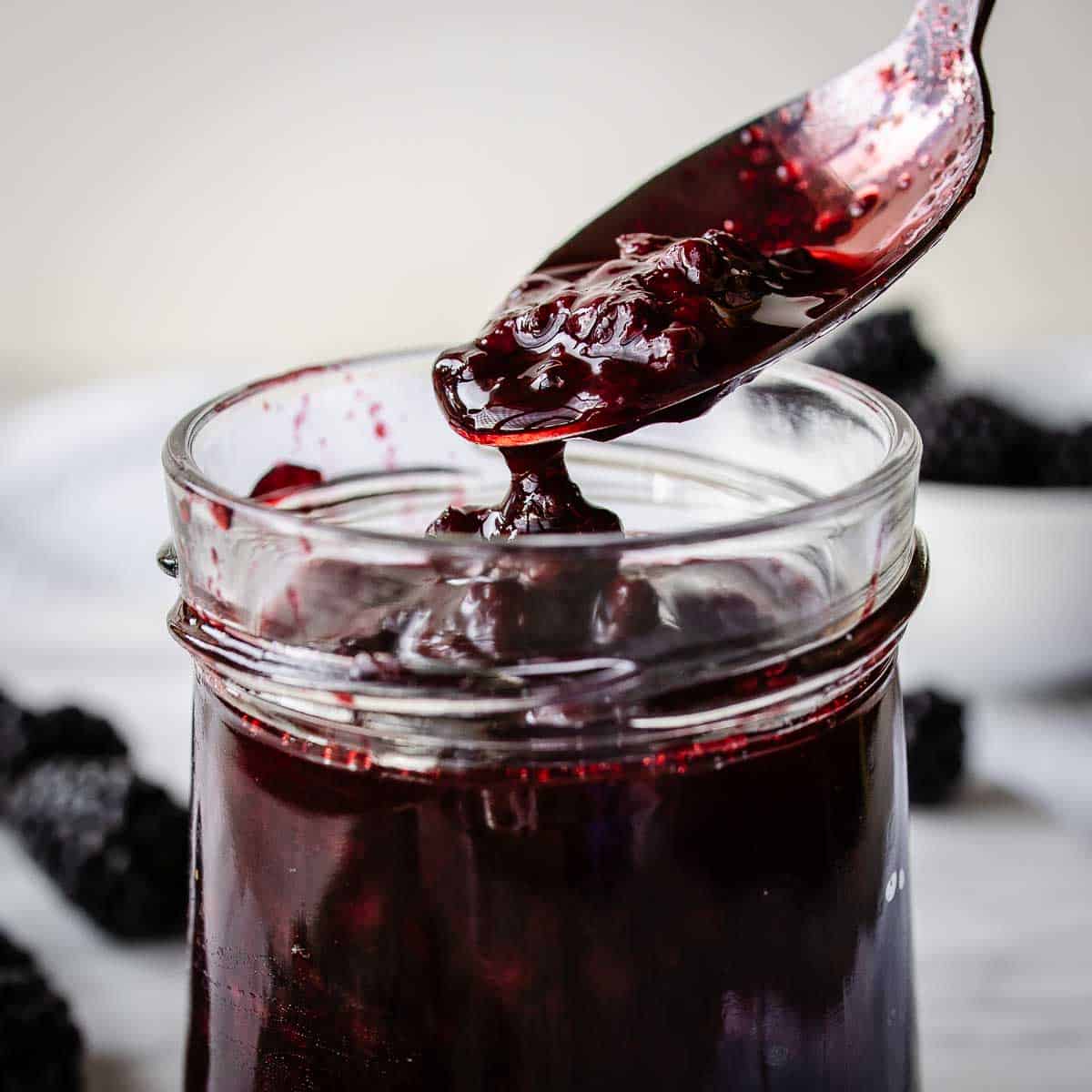 Blackberry compote being spooned into a glass jar.