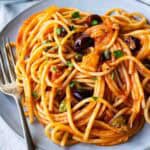 Plate of tuna pasta consisting of spaghetti in tomato sauce, with olives and chopped parsley.