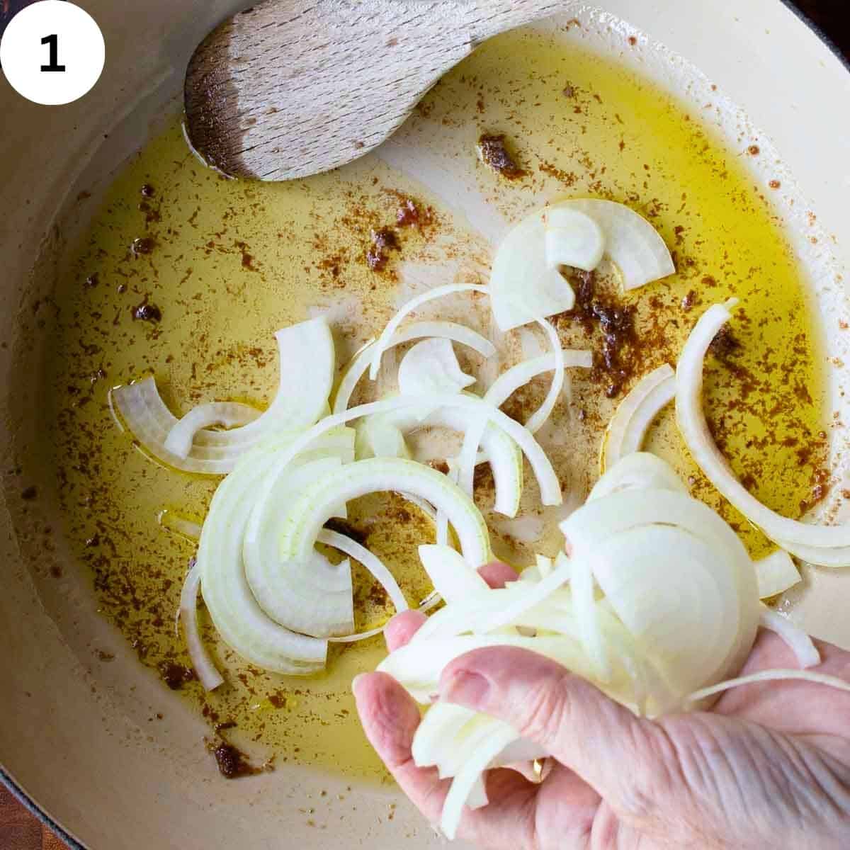 Sliced onions being added to a skillet.