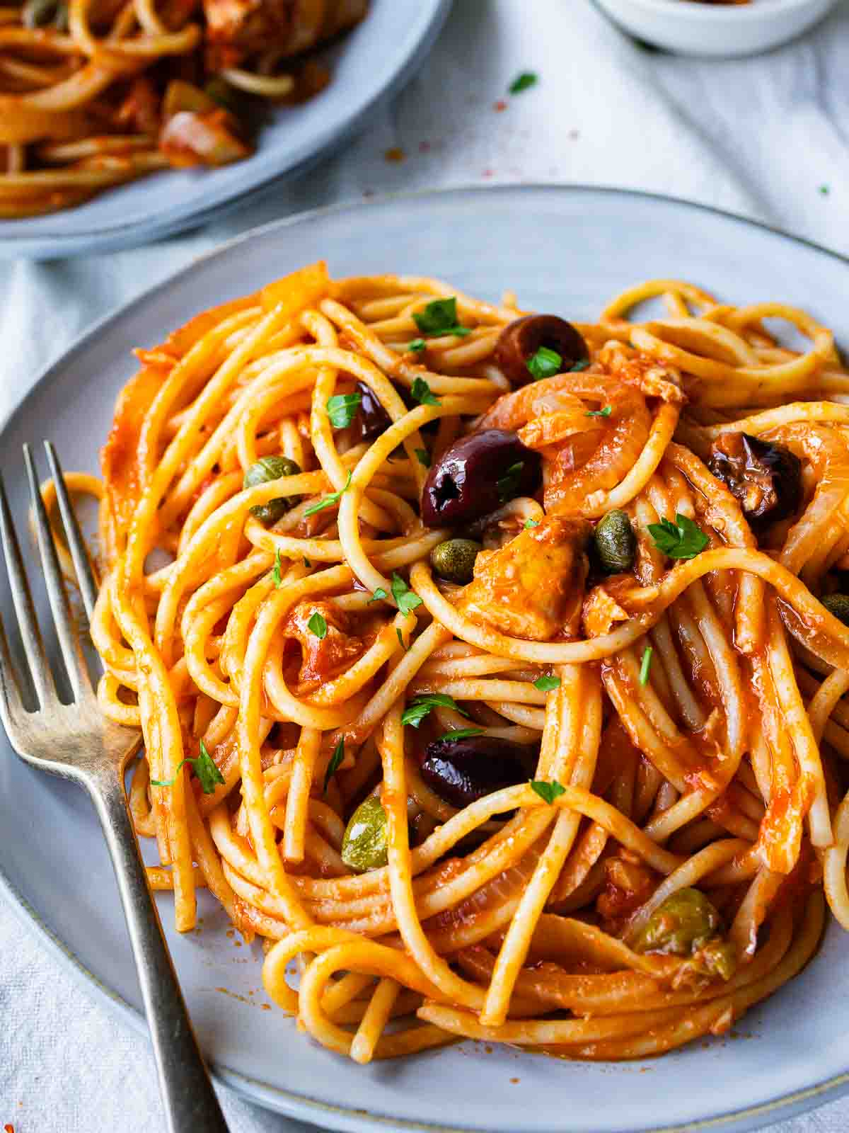 Plate of tuna pasta consisting of spaghetti in tomato sauce, with olives and chopped parsley.