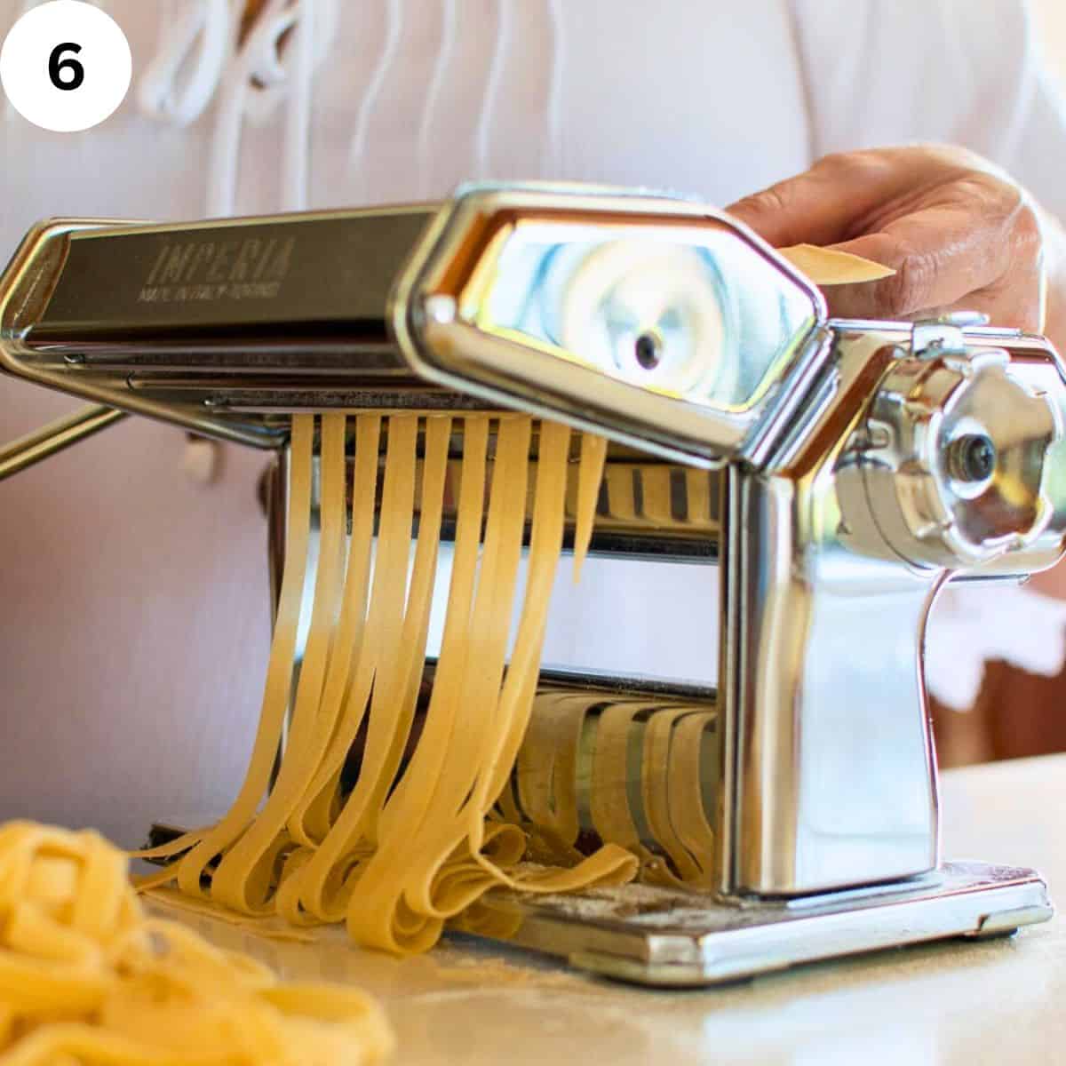Sheet of pasta dough being cut into tagliatelle using a pasta machine.