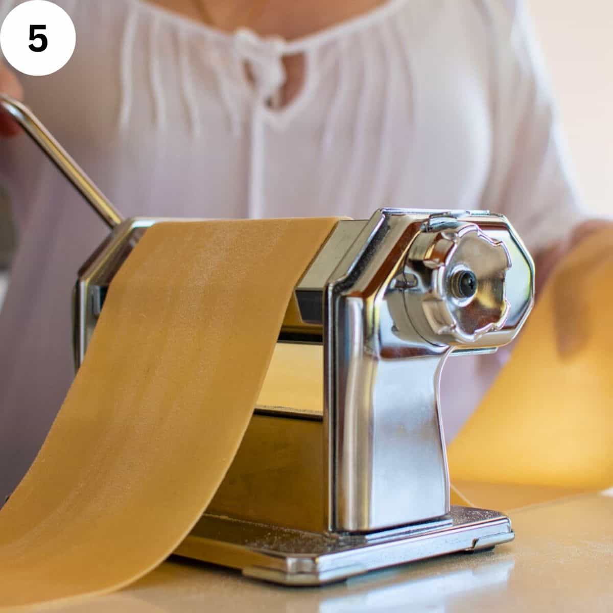 Pasta being rolled through a hand cranked pasta machine.