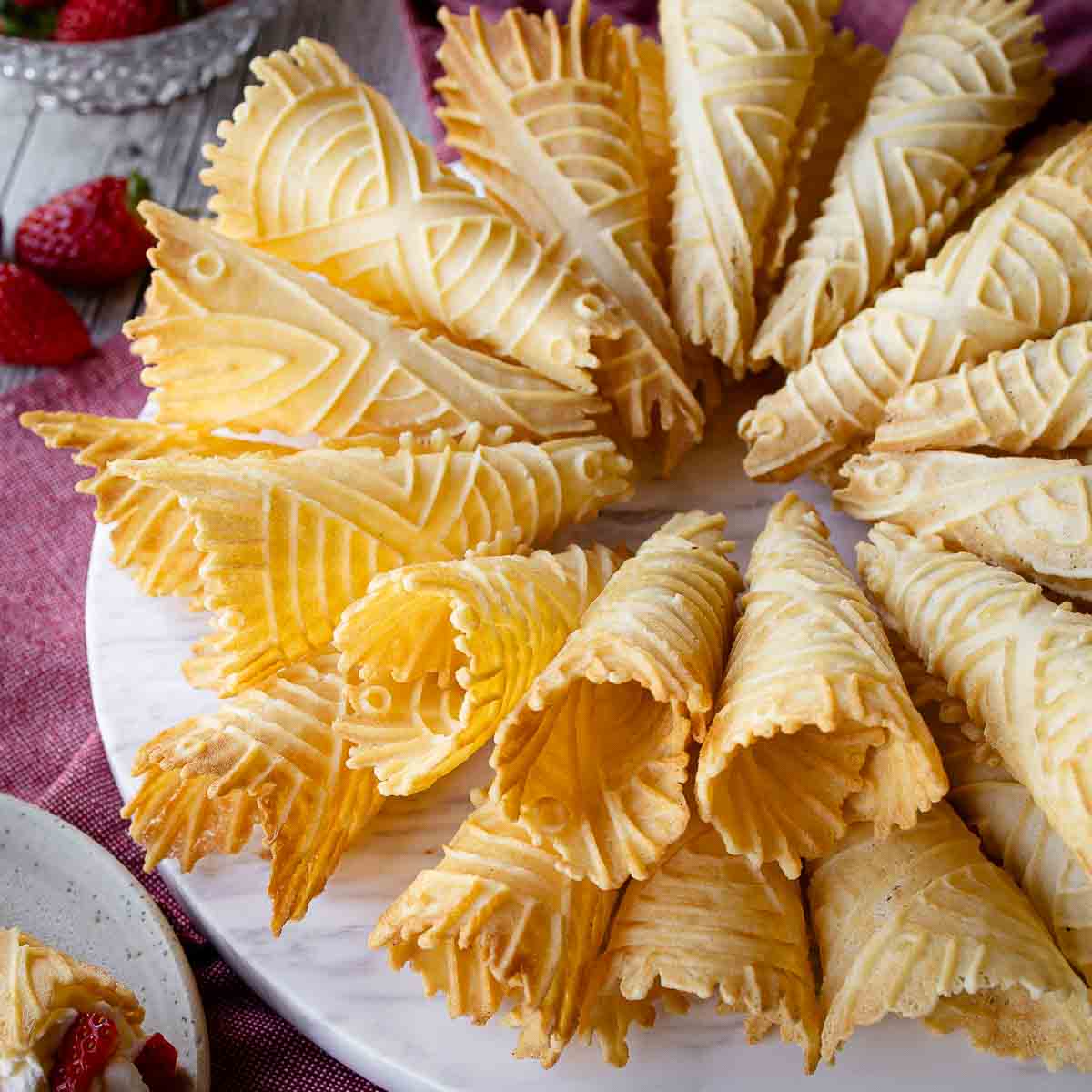A plate of krumkake with strawberries around it.